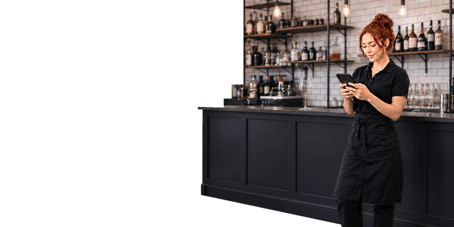 A restaurant server checking her phone in front of the bar, a single wine glass on the counter behind her